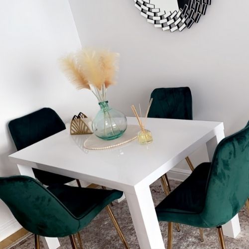 Modern bright dining room with rug, and white table with 4 green velvet chairs with fold legs and round wall mirror on shaggy grey rug