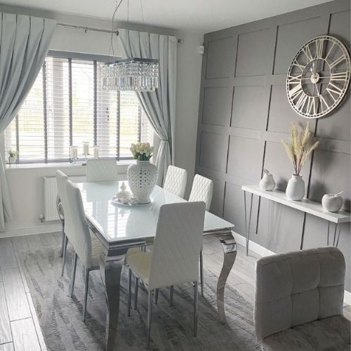 bright, modern white and grey dining area with white high gloss dining table with curled silver legs, and 6 white faux leather tall backed dining chairs, sat on a slightly textured grey rug.