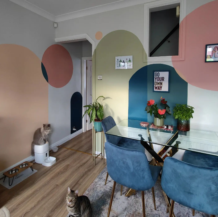 dopamine decor - modern eclectic dining room with glass and gold table and blue navy velvet chairs, with colourful spots of paint on the wall and two cats