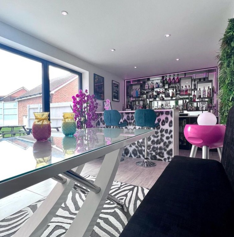 bold modern maximalist bar area with large french window, teal velvet barstools, white gloss dining table, leopard print design on wall and zebra print rug