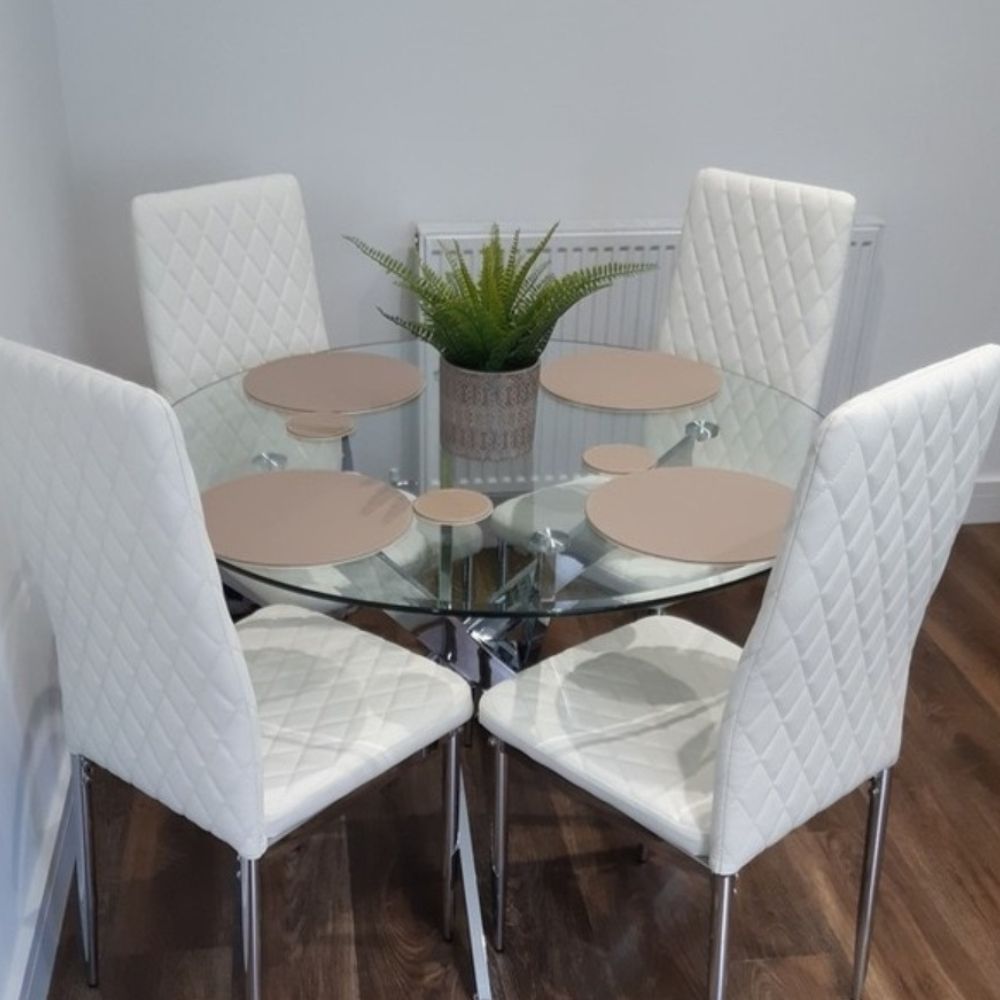 round glass dining table with solver chrome starburst legs, ad 4 white faux leather tall-back chairs in a white room