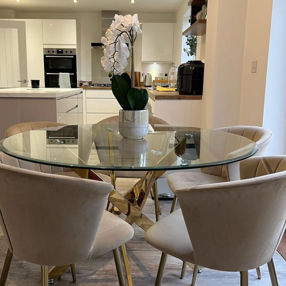 elegant round glass and gold metal dining table with 5 grey beige dining chairs with gold legs in grey and white dining area in open plan kitchen-diner, with white orchid on the table top.