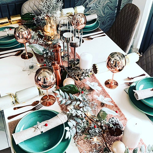 white table with rose gold runner, and tablescape of matching colours, and glasses, with green bowls and plates