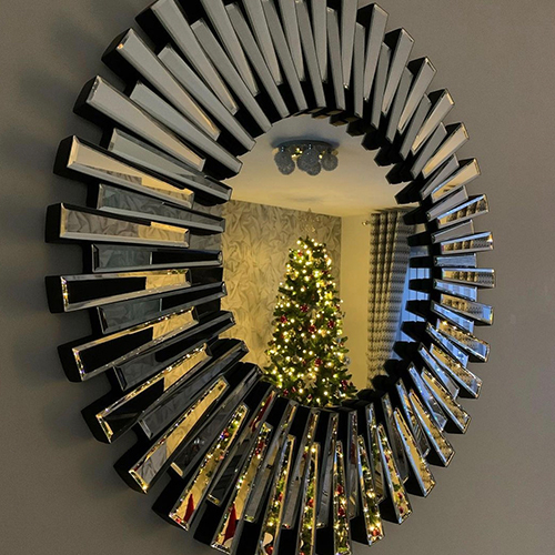 Round wall mirror showing reflection of Christmas tree.