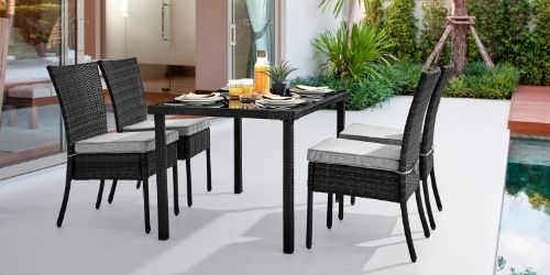 black rattan dining set comprising 4 tall back chairs with light grey cushions and 1 dining table with glass top. Pictured set up outside patio doors on stone terrace beside pool pond.