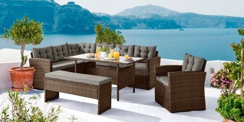 brown rattan outdoor dining set comprising chair,  seater bench and 6 seater sofa, oun outdoor white stone terrace overlooking sea