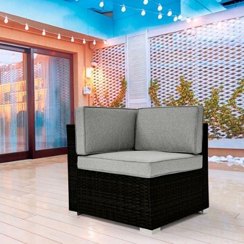 black rattan corenr armchair from teh Orlando range with lght grey cushions, pictured on decking outside patio doors, with white trellis behi and white fairy lights strung overhead