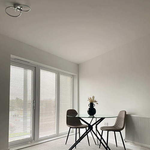 Modern dining area with industrial vibe featuring round glass dining table with balk metal hairpin legs and 2 beige faux leather chairs with black legs