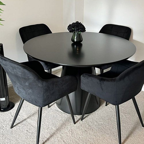 Black round table with tapered pedestal leg, and 4 black velvet dining chairs with arms and black tapered legs. 