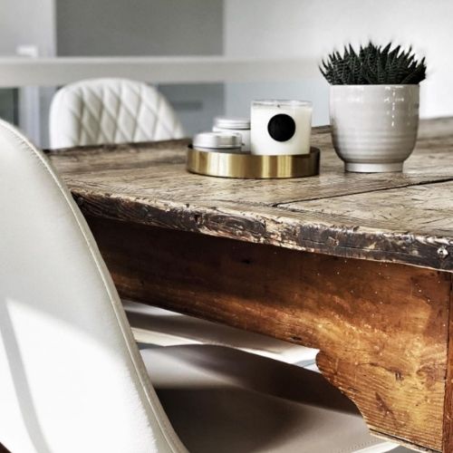 dark old wooden farmhouse table with white faux leather dining chairs and white accessories on tabletop