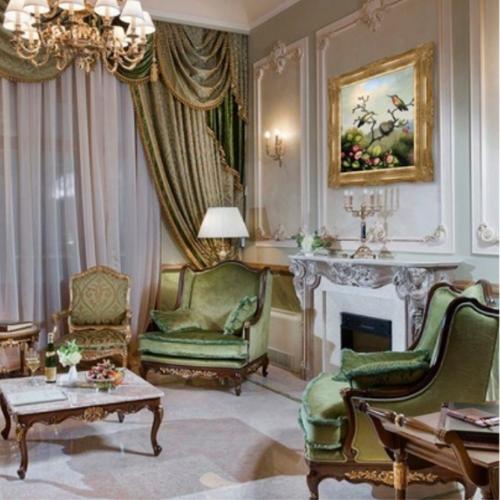 Regency Bridgerton style living room with heavy green velvet draps, green velvet furniture and ornate fireplace with gold accents.