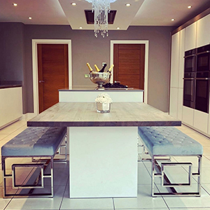 Danielle Lloyd's kitchen, showing central island with 2 grey velvet and silver chrome Cambridge bench seats from Furniturebox UK. Home renovation through flexible seating.