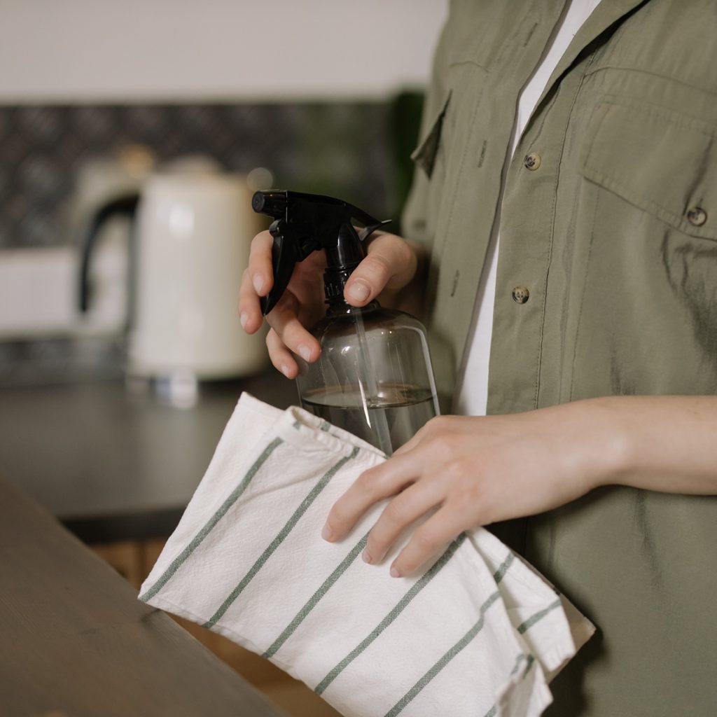 Image shows a person holding a spray bottle in one hand and a cloth in the other.