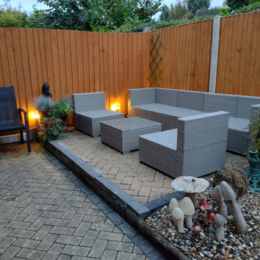 grey rattan garden furniture - modular soafa and armchairs with coffee table in raise paed patio area, with soft evening lighting. 