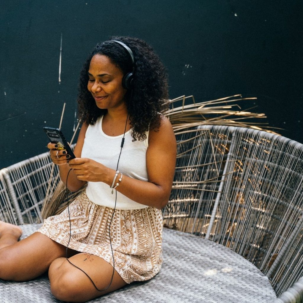 young Black woman sat in rattan moon chair listening to music and smiling