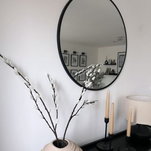 white wall with black framed round wall mirror, black console table and white accessories