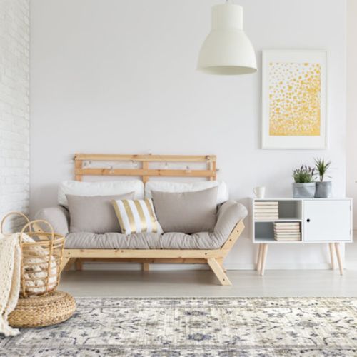 Scandi boho room with pale wood futon, shabby chic floral rug and yellow accessories