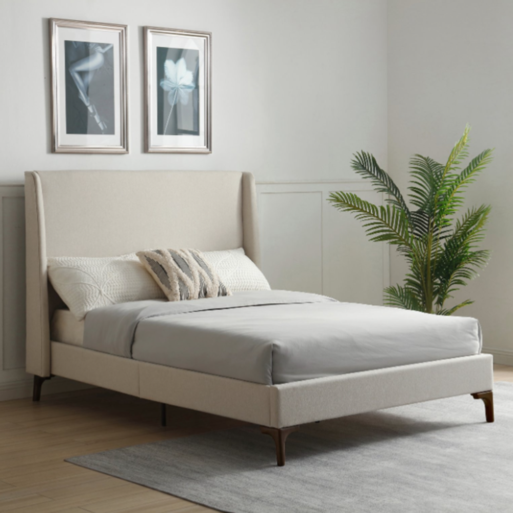 simple modern beige cream upholstered statement bed with tall headbaord and simple wings. on sturdy brown black metal legs in pale room with pot plant to left of bed.