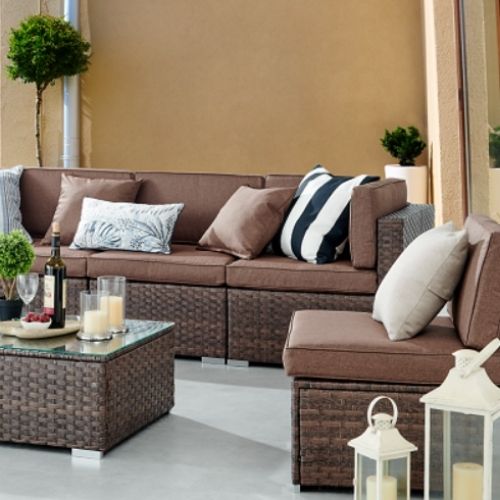 Garden Furniture Ideas For All Spaces blog - image shows modular brown rattan garden set with brown cushions arranged around a brown rattan coffee table with tmepered glass top, with wine glasses, bottles, candles and lanterns to accessorise