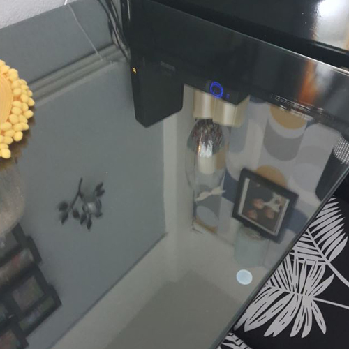 photo taken from above of dark dining table with glass table top protector on it. The walls and artwork of the room are reflected in the glass surface.