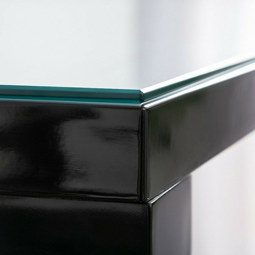 The corner of a black table with a glass table top protector on top