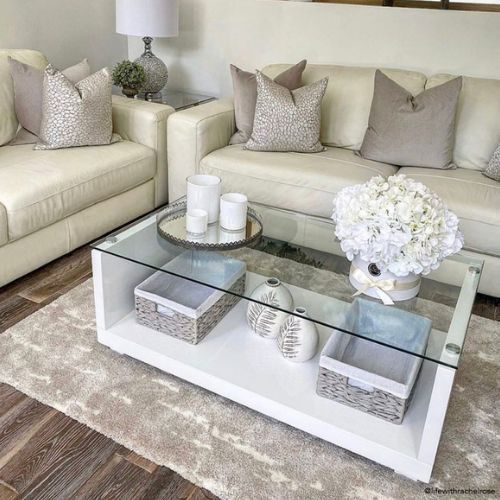  modern livng room with 2 sofas at 90 degrees with rectangular white high gloss and glass top coffee table. coffee table has 2 storage baskets on stroage shelf, and accessories on top.