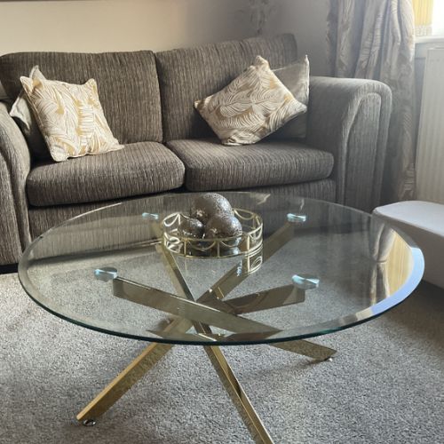 round clear glass coffee table with gold starburst legs in modern living room on grey carpet