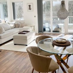 modern warm open plan living space with wooden floor, white sofa, round glass dining table with gold metal legs, and 4 beige velvet chairs with gold legs