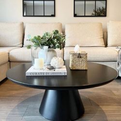 beige sofa and walls with black round pedestal coffee table and black window-mirrors on wall