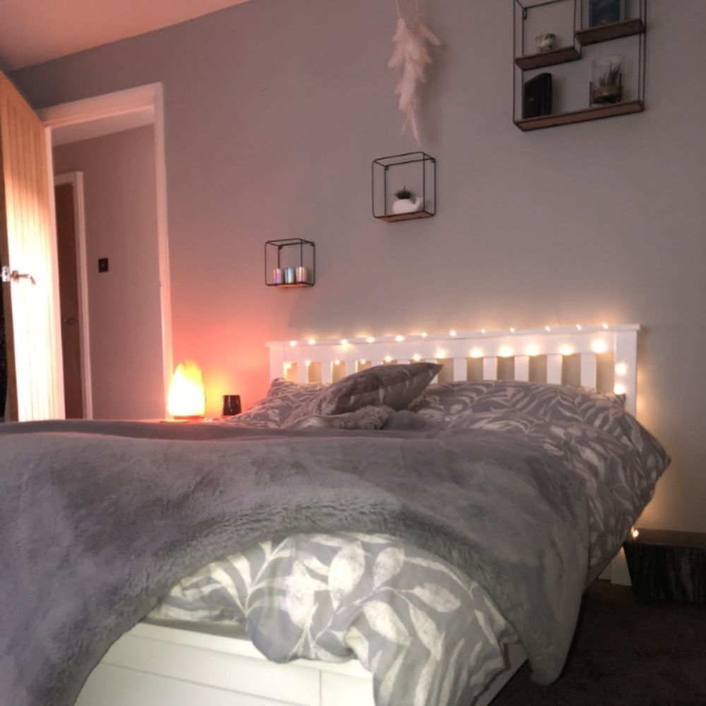 pretty pink and grey bedroom featuring solid white pine bed with fairy lights wrapped around headboard and soft glowing salt lamp on bedside table