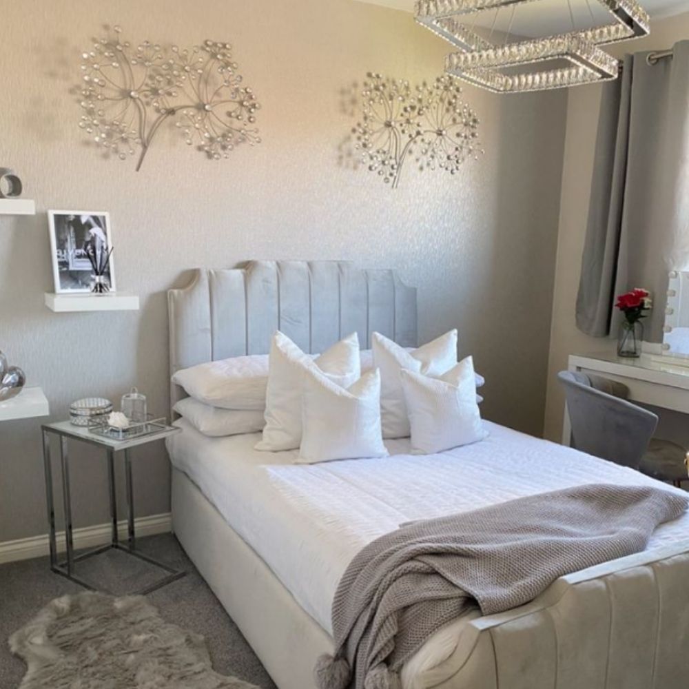 modern teenage bedroom in grey palette featuring luxury grey velvet bed with statement staggered headboard, white linens and grey blankets, with mirrored side table and floating shelves, with sparkly tree decal on wall. 
