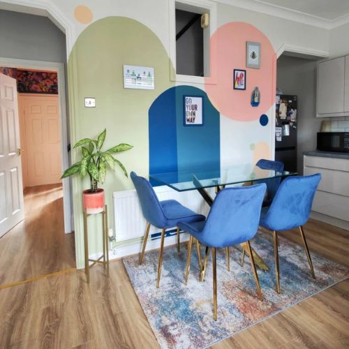 open plan kitchen dining area with glass dining table, blue velvet chairs and colured circles painted onto walls