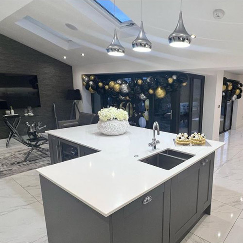 grey and white open plan living area wiht large cnetral ktichen island and glass and chrome concole and coffee table in background