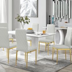 modern bright dining room featuring white high gloss dining table with 2 structural pillar legs and 6 white tall back faux leather chairs with diamond stitching and gold legs. 