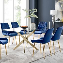 glass dining table with gold metal nested starburst legs and 6 navy blue velvet dining chairs with gold tapered legs.
