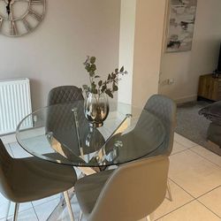 modern dining area with round glass dining table with chrome silver metal nested starburst legs and 4 faux leather grey dining chairs