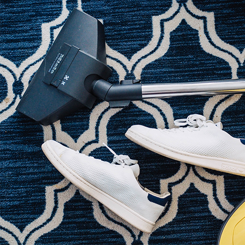 dark blue patterned rug witha  vacuum cleaner and a pair of shoes placed on top.