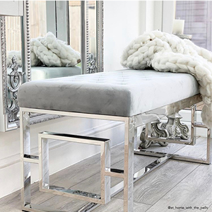 A silver and grey velvet bench in a hallway below a large silver mirror