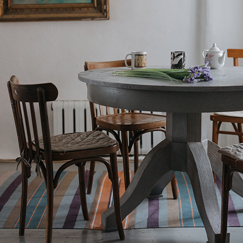 Mismatched table and collection of wooden dining chairs on a thin low pile colourful stripey rug.