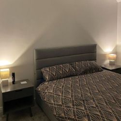 modern bedroom with grey faux leather bedframe and 2 grey wooden scandi style bedside tables with square lamps. 