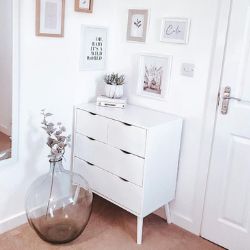 white wooden chest of drawers with flat fronts, no handle, super minimalist Scandiavian inspired design, 2 wide drawers and 2 smaller drawers. In corner of room beside large glass vase. Gallery wall behind. 