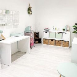 white modern room featuring simple white gloss desk, hanging pegboards, and square shelving unit against back wall with storage boxes & baskets