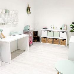 white modern room featuring simple white gloss desk, hanging pegboards, and square shelving unit against back wall with storage boxes & baskets