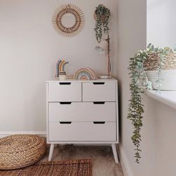 white Alma chest of drawers from Funriturebox, in corner of childs bedroom with rainbow toys on the top, lamp round wicker fame mirror and trailing pot plants. 