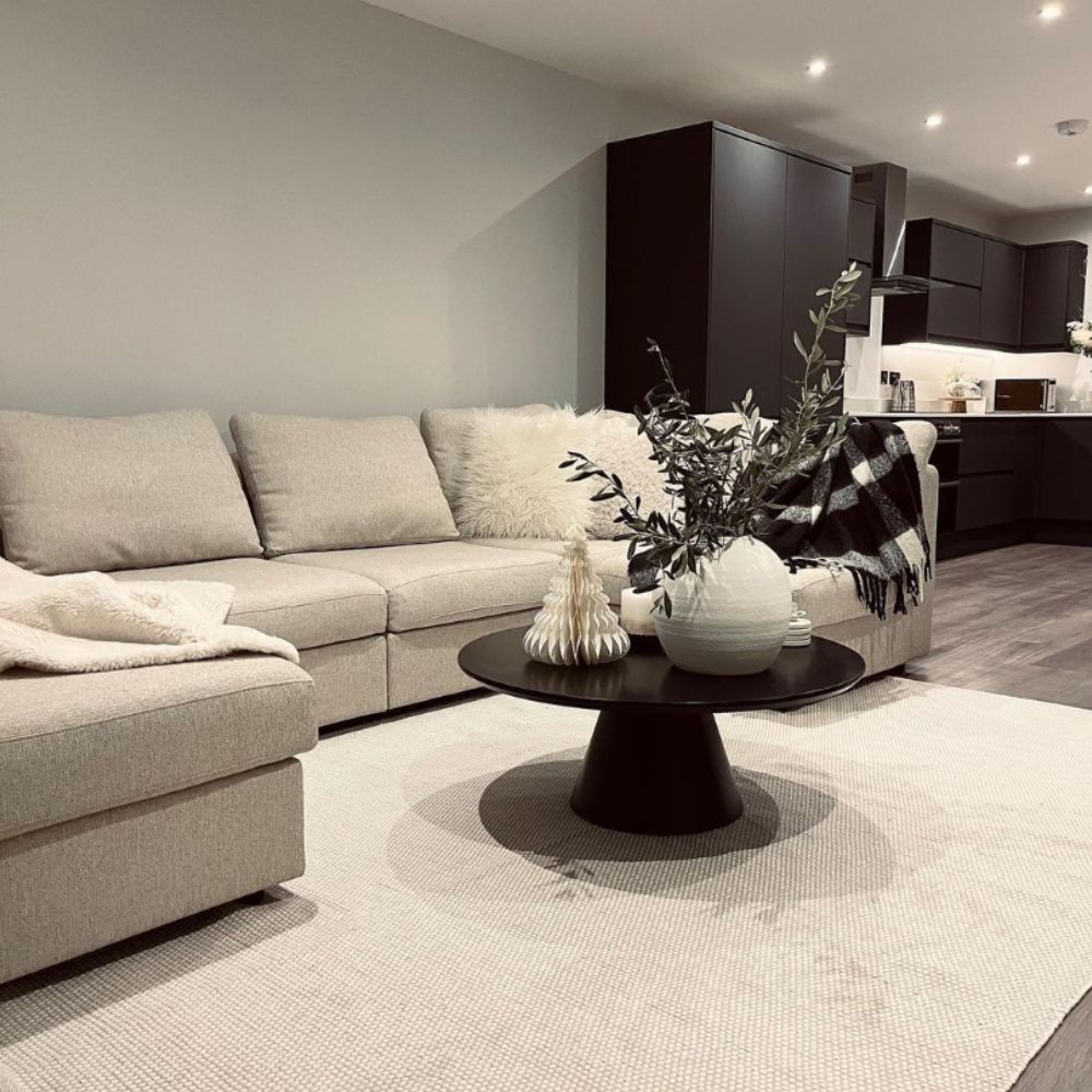 modern lopen plan living room and kitchen space with cream rug and cream sofa in foreground with black round coffee table with a large statement tapered central pillar