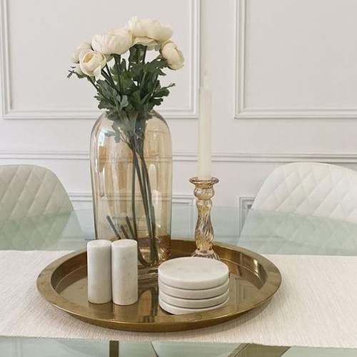 round glass table with gold chrome legs, white leather chairs. white table runner, gold tray, white and gold accessories, white roses in vase
