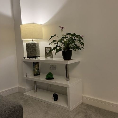 3 shelf console unit in white gloss with chrome supports. In corner of room, with lamp and accessories.