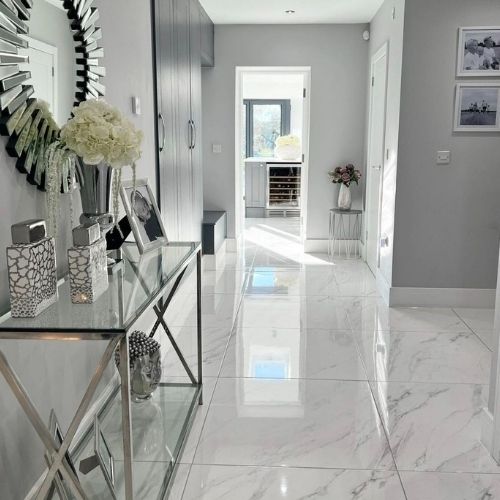 bright and light modern entrance hall with white marble effect floor tiling, glass and chrome console table and round wall mirror with mirrored frame. 