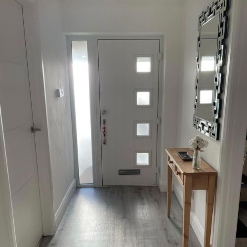 modern entrance hallway with front door, light wooden console table and large rectangular wall mirror in mirrored frame hung vertically above it,