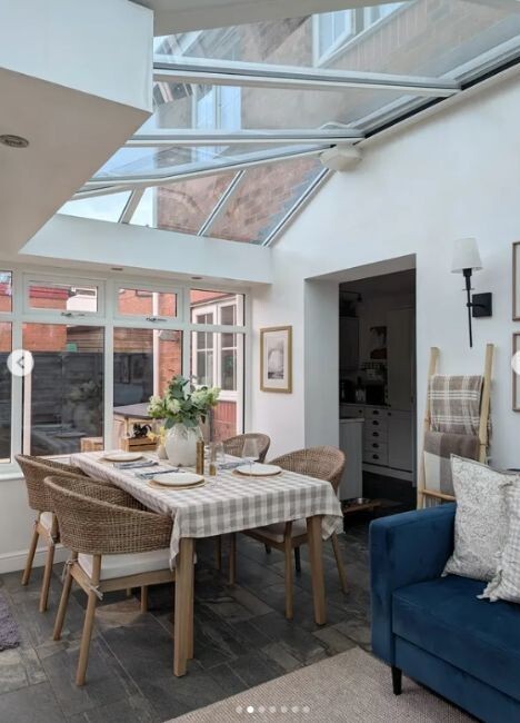 Wood & wicker stackable dining chairs at a wood dining table in a conservatory living space beside sofa
